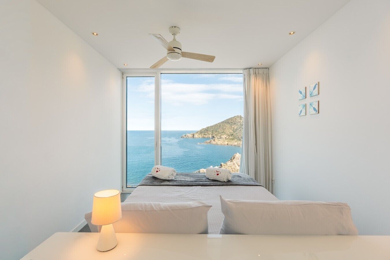 Une chambre avec un lit, une lampe de chevet, un ventilateur de plafond et une vue sur la mer.