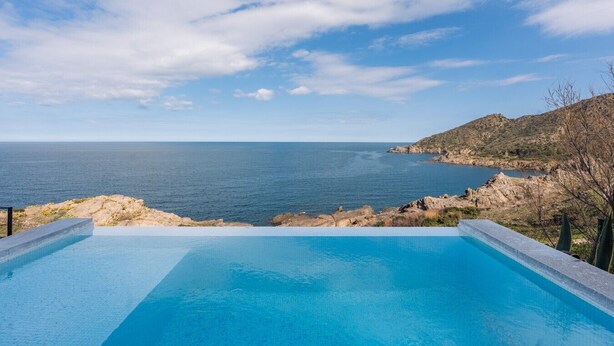 Ein klares, blaues Schwimmbecken mit Blick auf das Meer und eine felsige Landschaft.