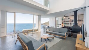 Ein modernes Wohnzimmer mit großem Fenster zum Meer, einem Kamin und einem Bücherregal.