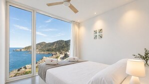 Ein Schlafzimmer mit großem Fenster, einem Bett, einem Deckenventilator und einer Nachttischlampe.
