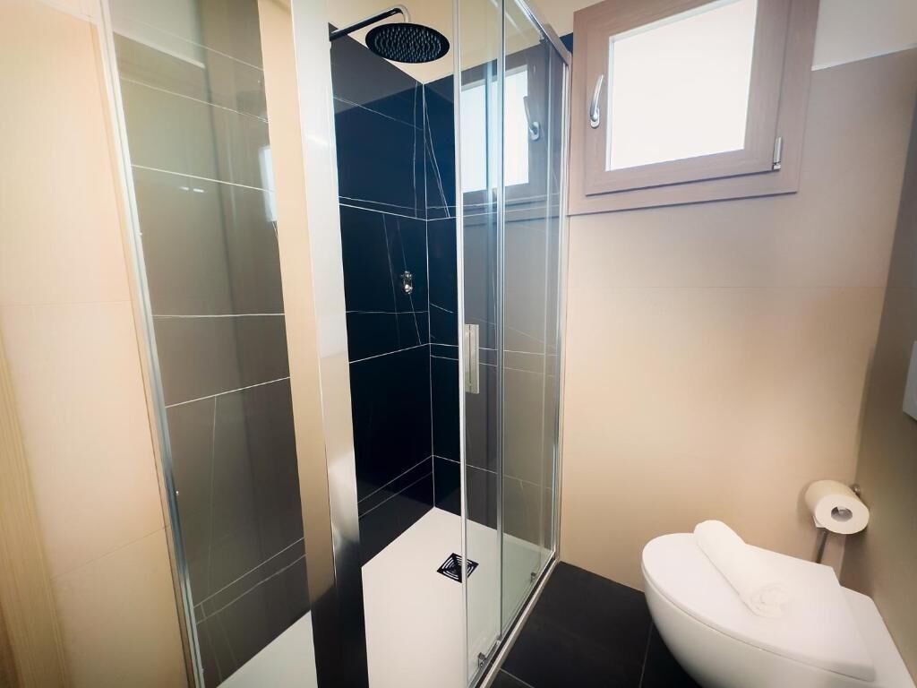 Un baño moderno con ducha de vidrio, inodoro blanco y pared con azulejos color crema.