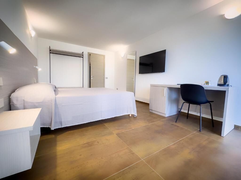 Een moderne slaapkamer met een bed, bureau, stoel en een televisie.