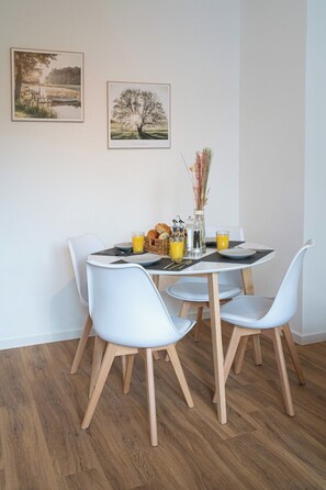 Un coin repas avec une table ronde, des chaises blanches et un vase contenant des fleurs séchées.