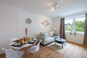 Ein modernes Wohnzimmer mit Essbereich, einer Couch, einem Couchtisch und einem großen Fenster mit Vorhängen.