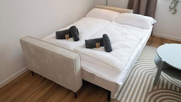 A bed with white bedding, two rolled towels, a small chair, and a round table.