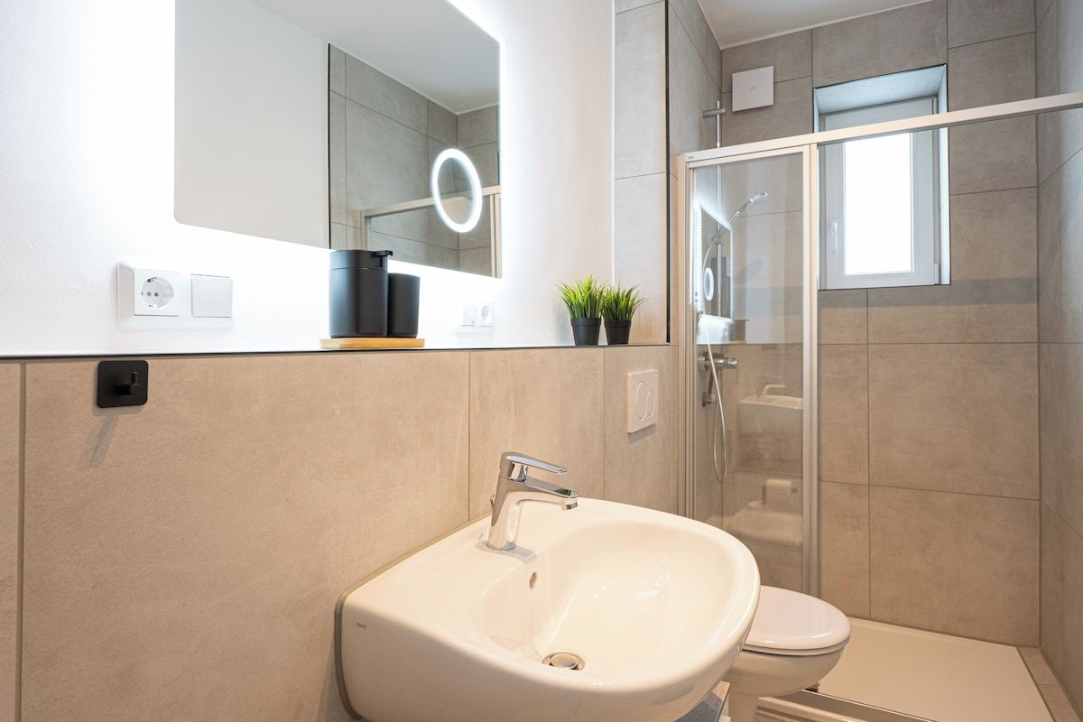 Ein modernes Badezimmer mit Waschbecken, Spiegel mit Beleuchtung, Toilette und Duschbereich.