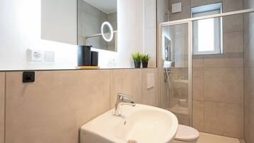 Ein modernes Badezimmer mit Waschbecken, Spiegel mit Beleuchtung, Toilette und Duschbereich.