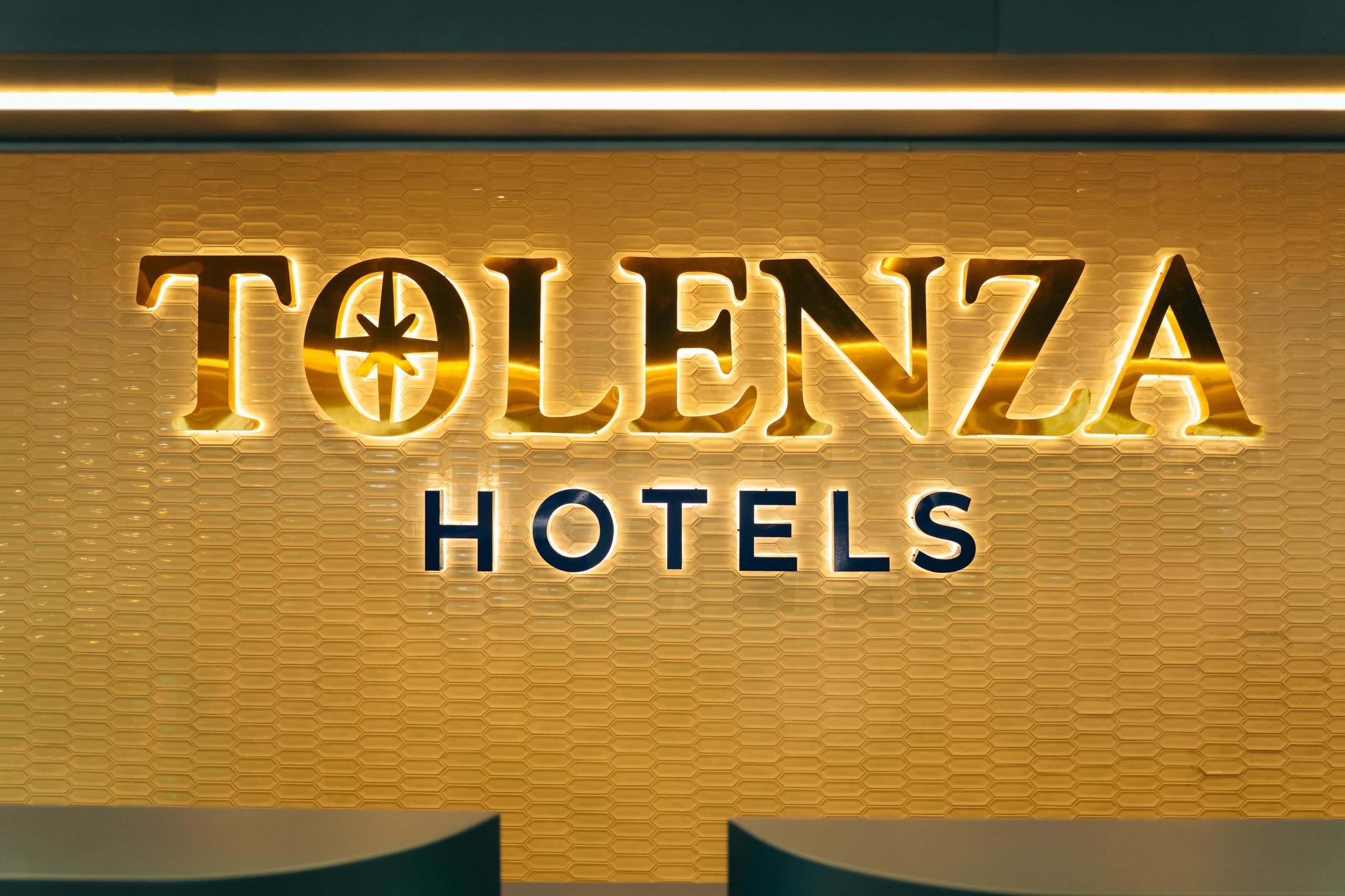 Een hotelsbord met de naam 'TOLENZA HOTELS' verlicht in een modern lettertype.