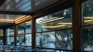 Un restaurant dont l’intérieur est aménagé avec des tables et des chaises, de grandes fenêtres et un plafond équipé de luminaires linéaires.