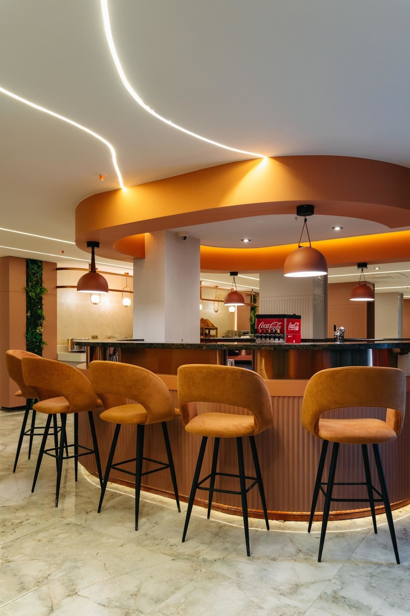 Un espace bar doté d’un comptoir incurvé, de quatre tabourets de bar, d’un éclairage suspendu et d’un réfrigérateur Coca-Cola.