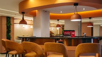 Un espace bar doté d’un comptoir incurvé, de quatre tabourets de bar, d’un éclairage suspendu et d’un réfrigérateur Coca-Cola.