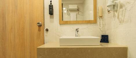Un baño con puerta de madera, lavamanos de mármol, espejo, secador de manos y teléfono.