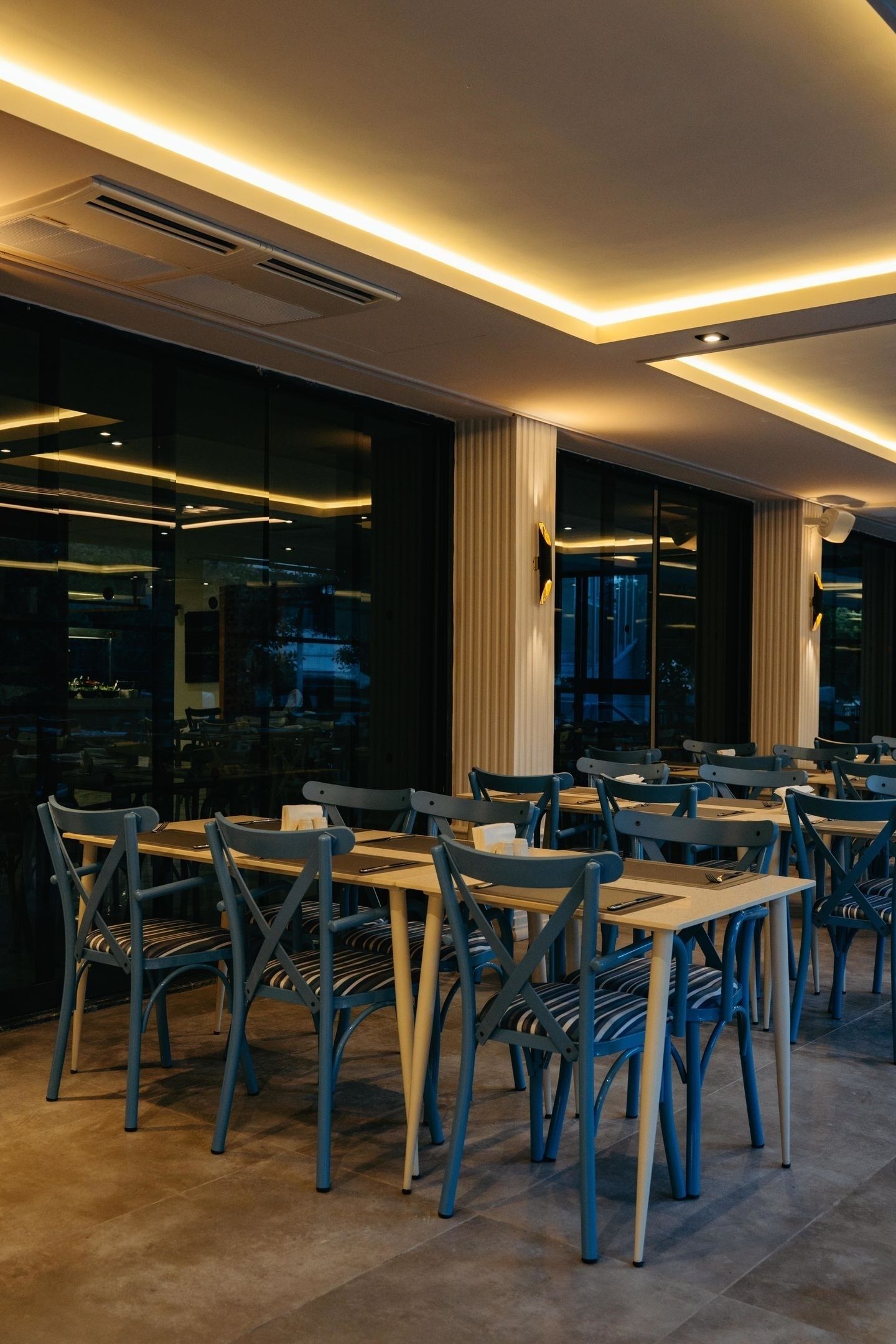 A modern dining area with tables and chairs, large windows, and recessed ceiling lighting.