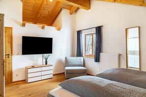 Une pièce avec un lit, une chaise, un téléviseur, une fenêtre avec des rideaux et un plafond en bois.