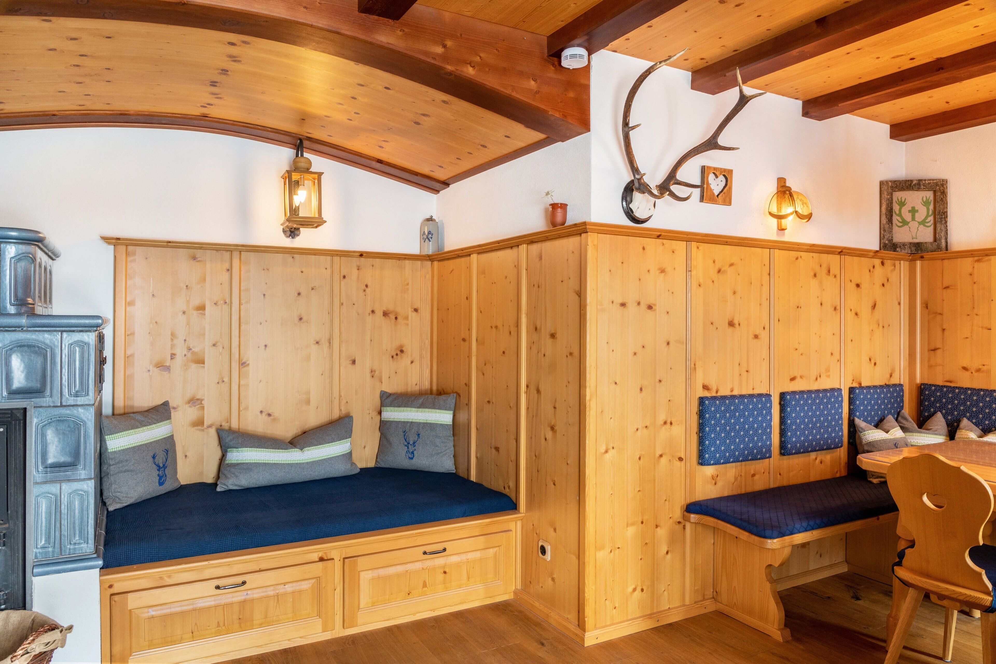 Interno di una baita in legno con una panca, un tavolo e un corno di cervo appeso al muro.