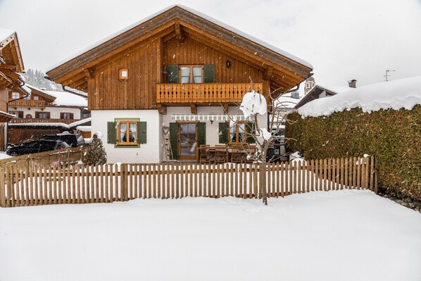 Un chalet en bois doté d’un balcon, d’un coin repas et d’un jardin recouvert de neige.
