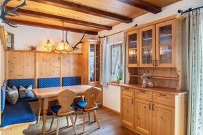 L’intérieur d’un chalet en bois comprend une table à manger, des chaises, un banc avec des coussins, un coin cuisine avec des placards et un luminaire suspendu.