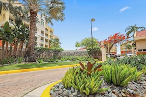A hotel entrance with a paved pathway, palm trees, and a well-maintained garden.