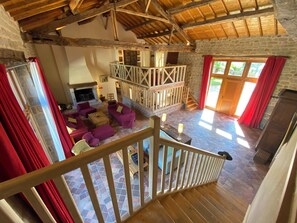 Un vaste espace de vie agrémenté d’une cheminée en pierre, de poutres apparentes en bois et d’un balcon doté d’une balustrade en bois.