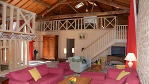 Amplia sala de estar con vigas de madera, una escalera y un televisor.
