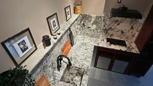 Un baño con encimera de mármol, lavabo, espejo, cuadros enmarcados y una planta.