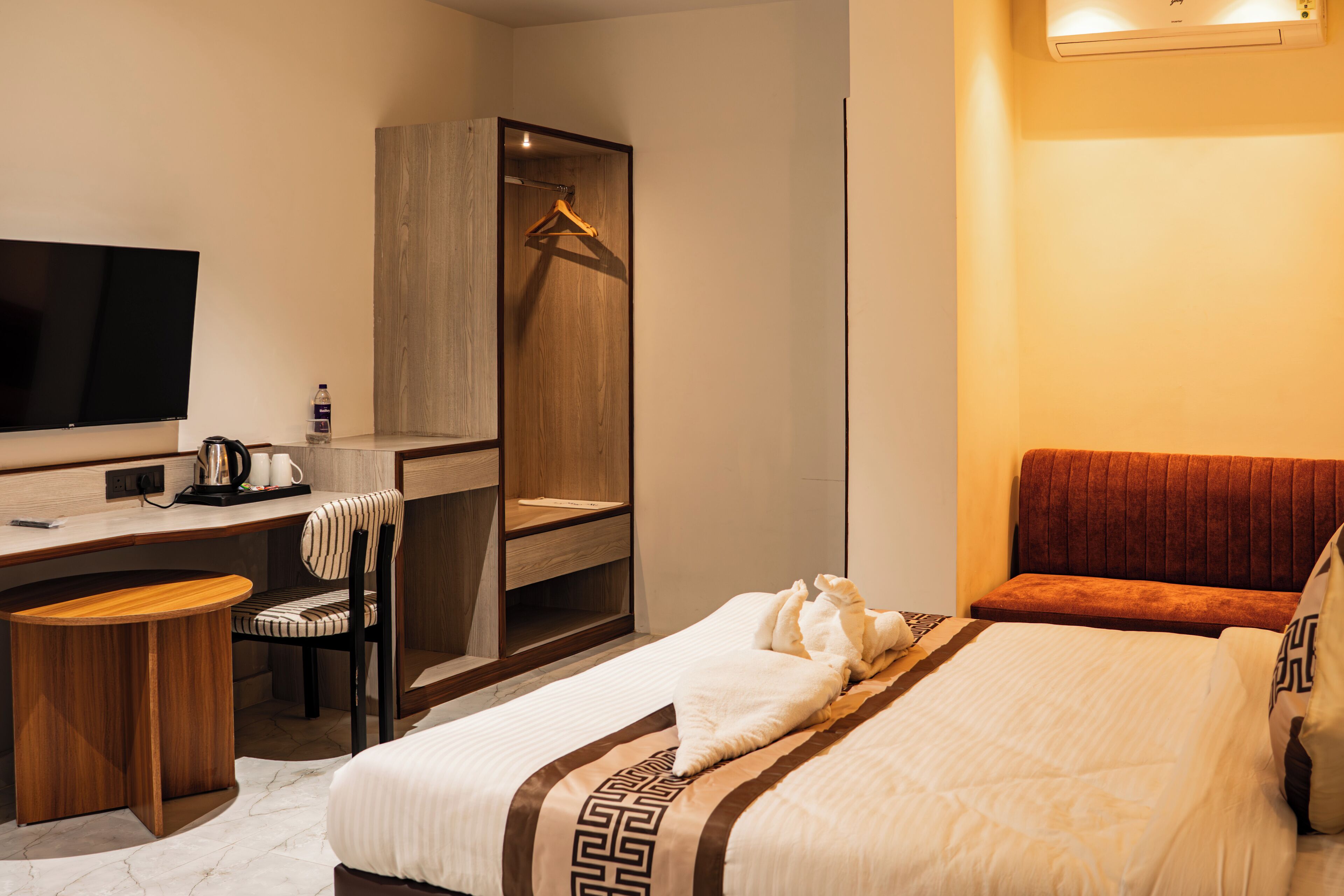A hotel room with a bed, a desk, a chair, a TV, and a wardrobe.