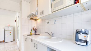 Et moderne køkken med hvide skabe, en dobbeltvask, kaffemaskine og et køleskab.