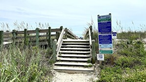Una scala di legno conduce a una spiaggia, con un cartello che illustra le norme balneari e un codice QR per maggiori informazioni.