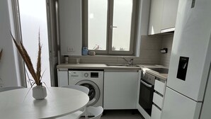 A modern kitchen with white cabinetry, a built-in oven, and a dishwasher. There is a window above the sink, and a dining area with a round table and chairs. - Eidolion Essence Nest - Mykonos Cozy Getaway (Mykonos)