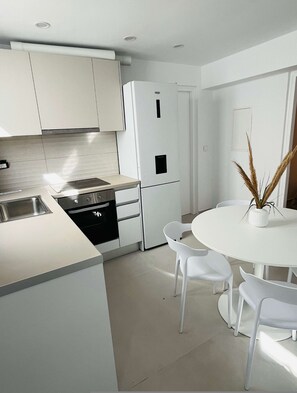 A modern kitchen with white cabinetry, a built-in oven, and a white dining table with chairs. - Eidolion Essence Nest - Mykonos Cozy Getaway (Mykonos)
