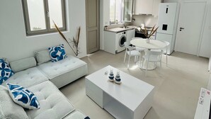A modern living room with a sofa, coffee table, and a dining area with chairs. - Eidolion Essence Nest - Mykonos Cozy Getaway (Mykonos)