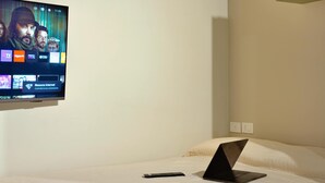 Habitación de hotel con una cama, una laptop sobre la cama y un televisor en la pared mostrando la interfaz de un canal.