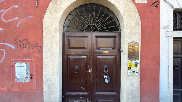 Una puerta doble marrón con un arco de metal encima, ubicada en una pared roja con grafitis y un letrero con el número '88'.