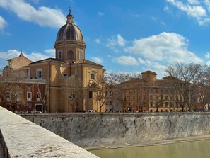 A historic building with a prominent dome and classical architecture, situated by a river with a stone wall in the foreground. - Il Borghetto old Town gem (Rome)
