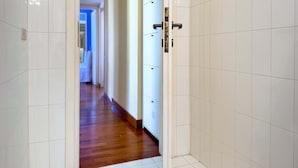 Un pasillo con paredes de baldosas blancas y suelo de madera, que conduce a una habitación con una puerta.