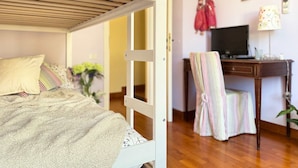 Una litera con escritorio y silla, un televisor y un estante con objetos decorativos.