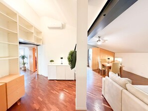 A modern apartment with a wooden floor, a dining area with a table and chairs, a white cabinet, and a ceiling fan. - Loft Piazza Maggiore Comfort in the City Center (Bologna)