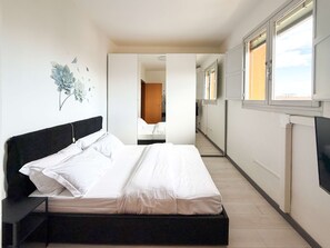 Een slaapkamer met een bed, een nachtkastje, een aan de muur bevestigde televisie en een deur naar een andere kamer.