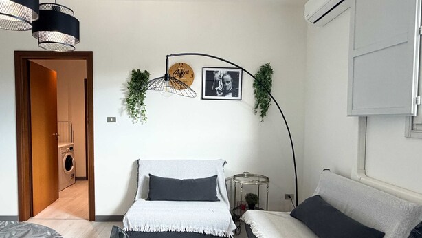 A modern bedroom with a bed, a sofa, a hanging light fixture, a clock, and a small plant. - Cinzia s City Pad Comfort Near Central Station (Bologna)