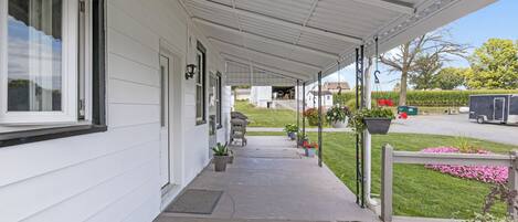 A covered porch with a wooden deck, potted plants, and a view of a house and street.
