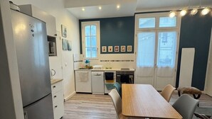 Een kleine keuken met een koelkast, een eettafel met stoelen en een klein aanrecht met een spoelbak.
