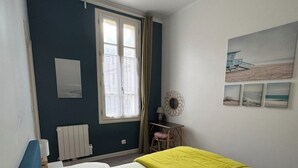 Een slaapkamer met een bed, een raam, een radiator, een stoel en een muur met foto's.