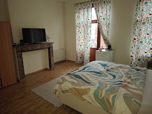 A bedroom with a bed, a desk with a TV, a radiator, and floral curtains.
