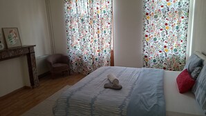 A bedroom with a bed, a chair, a radiator, and curtains with a floral pattern. - Large, bright bedroom (Molenbeek)