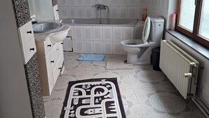 A bathroom with a bathtub, toilet, sink, and a window. - Large, bright bedroom (Molenbeek)