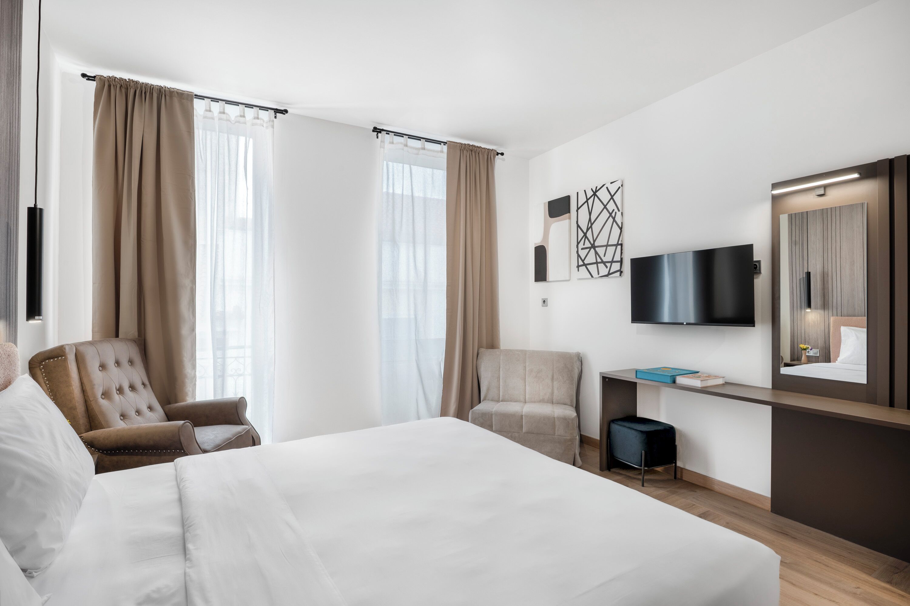 A hotel room with a large bed, two armchairs, a desk with a flat-screen TV, and a mirror.