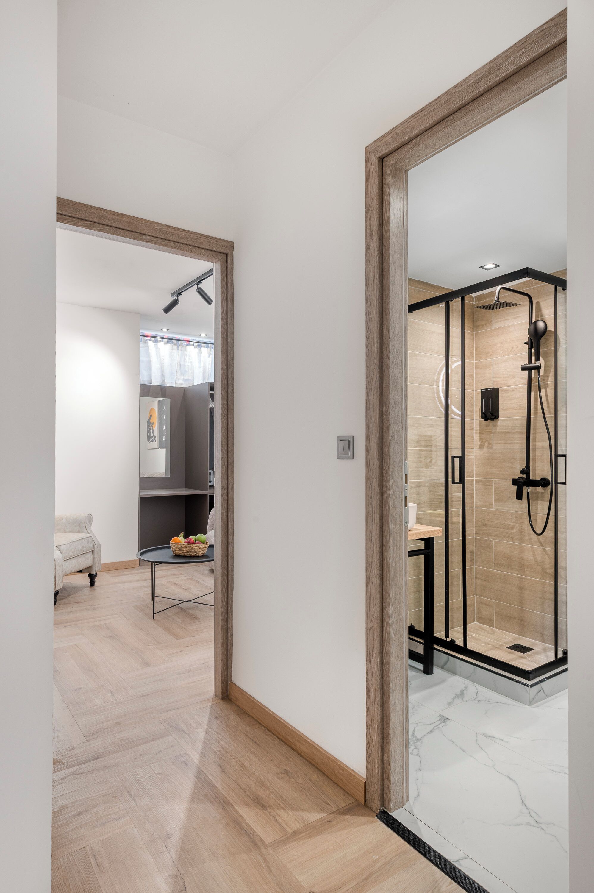 A modern bathroom with a glass shower enclosure, a marble floor, and a wooden-framed door.