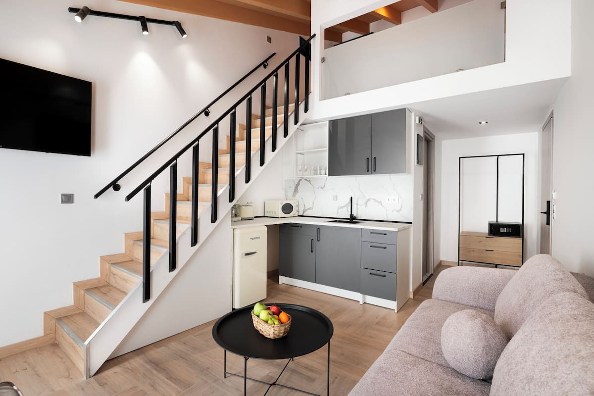 A modern apartment with a staircase, kitchen, living area, and a flat-screen TV.