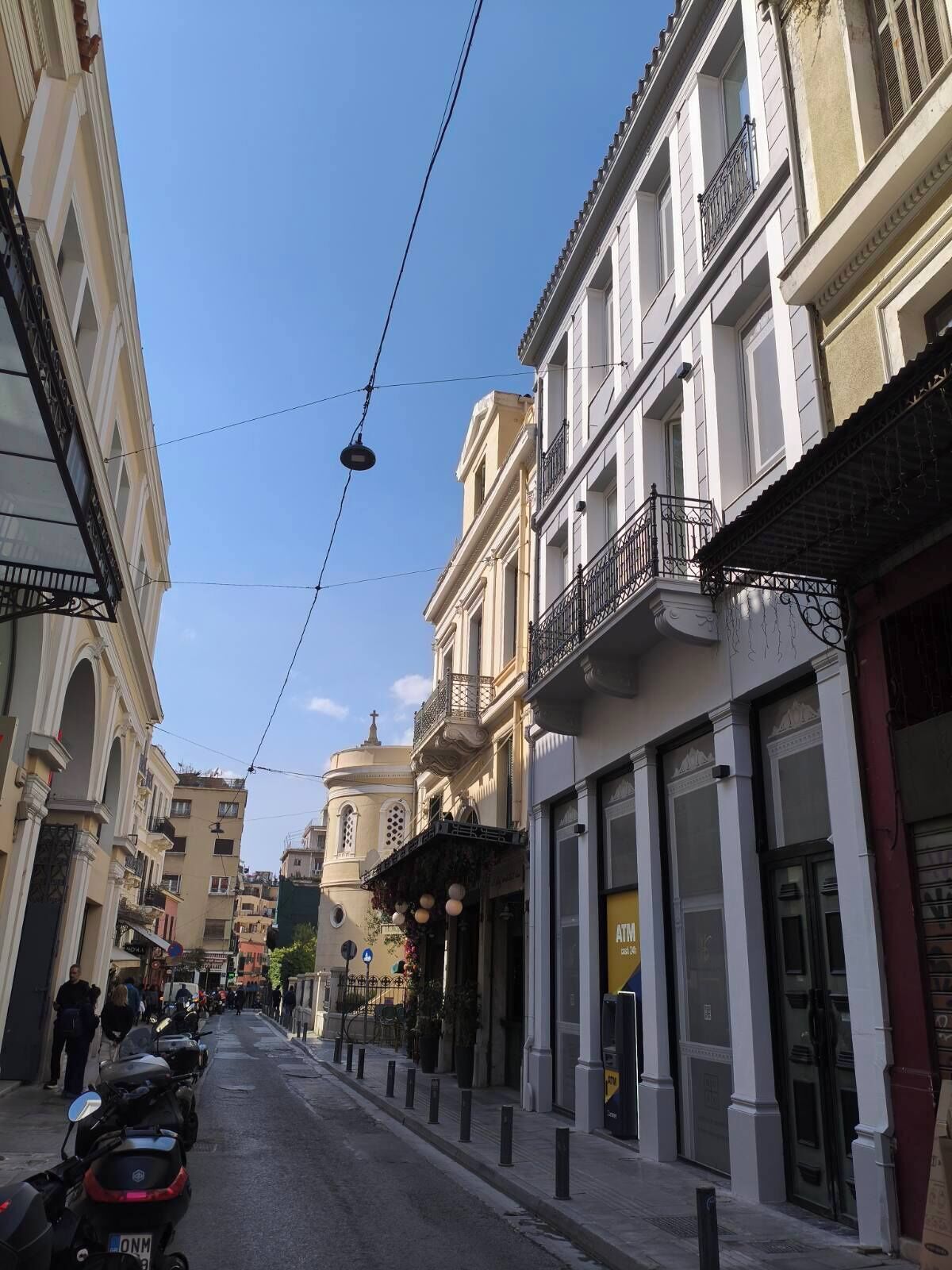 Une rue bordée d’immeubles, un ciel dégagé et une église surmontée d’un dôme.