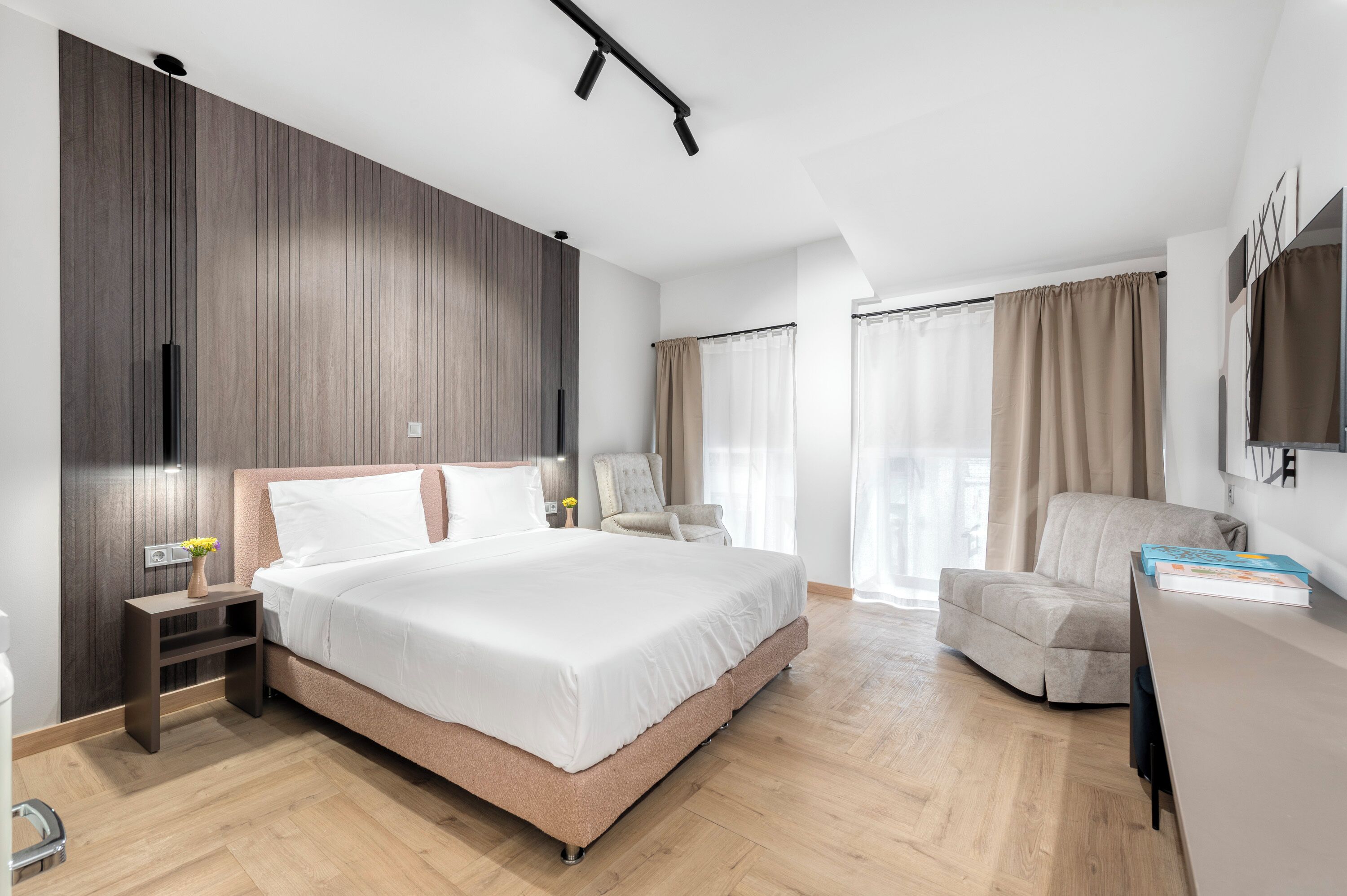 Une chambre d’hôtel moderne, dotée d’un grand lit, d’un bureau, d’une chaise et d’un téléviseur fixé au mur.